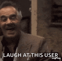 a man in a suit is laughing and pointing at the camera .