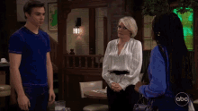 a man in a blue shirt stands next to a woman in a white blouse with abc written on the bottom left