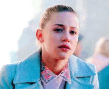 a close up of a woman 's face wearing a blue jacket and a floral shirt .