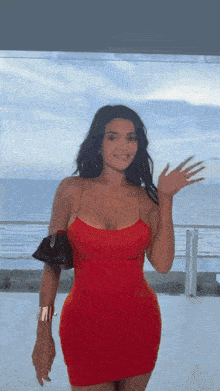 a woman in a red dress is standing in front of a body of water .
