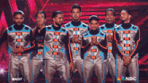 a group of men standing on a stage with the nbc logo on the bottom right