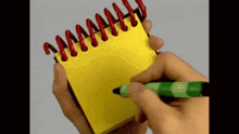 a person is writing in a yellow notebook with a green marker