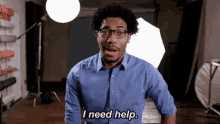 a man wearing glasses and a blue shirt says " i need help "