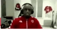 a man wearing headphones and a red jacket is talking on a video call in a dressing room .