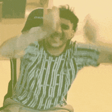 a man in a striped shirt is sitting on a chair with his arms in the air .