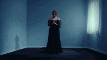 a woman in a long black dress is standing in a corner of a room