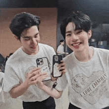 two young men are standing next to each other and smiling while holding a cell phone .