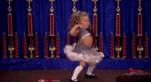 a little girl in a tutu is dancing in front of trophies .