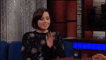 a woman in a sequined sweater applauds while sitting in front of a mug that says abc