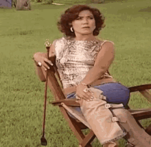 a woman is sitting in a wooden chair holding a cane in a field .