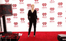 a woman stands on a red carpet in front of a wall with hearts on it