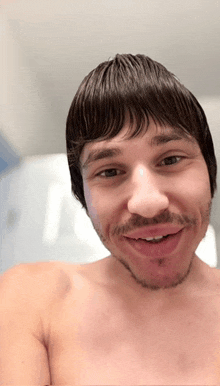 a shirtless man with a wig on his head smiles for the camera
