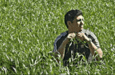 a man in an adidas shirt is sitting in a field of tall grass .