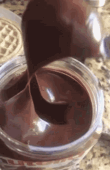 a jar of chocolate spread is being poured into a cup on a counter .