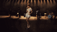 a woman singing into a microphone in front of a drum set