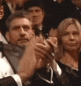 a man in a tuxedo and bow tie is applauding in a crowd of people .