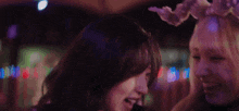 two women are standing next to each other in a dark room and one has a flower crown on her head