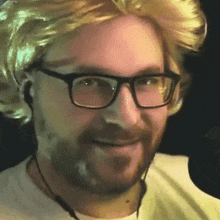 a man wearing glasses and a blonde wig smiles for the camera