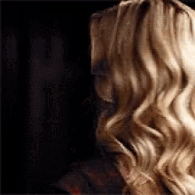a woman with long blonde hair is standing in front of a black curtain .