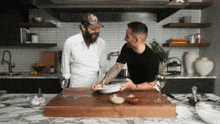 two men are in a kitchen preparing food and one has a beard