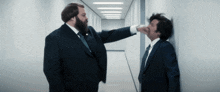 a man in a suit is slapping another man in a hallway