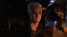 a man with a shaved head is standing in a dark room with a woman behind him .