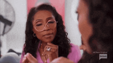 a woman wearing glasses and a pink shirt is looking at another woman .