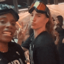 a man wearing goggles is giving a peace sign next to a man wearing a black shirt that says ' a '