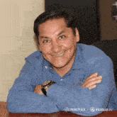 a man wearing a blue shirt and a watch sits at a table