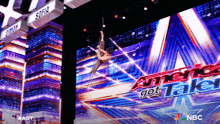 a woman is hanging from a rope in front of a large screen that says america got talent