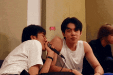 a man kissing another man on the cheek while holding a microphone with a heart sticker on the wall behind them