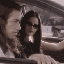 a woman wearing sunglasses sits in a car with a man