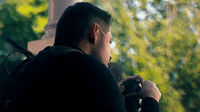 a man with a backpack is taking a picture with a camera in a park .
