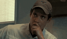 a man wearing a baseball cap is sitting at a table with his hand to his chin .