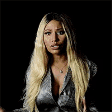 a woman with long blonde hair and a plunging neckline is wearing a silver jacket .