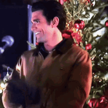 a man standing in front of a christmas tree smiling