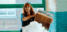 a woman with red hair is holding a cardboard box with a picture on it