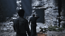 two men are standing in a dark cave looking at a stone wall