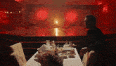 a man is sitting at a table in a dark room with a red light behind him .