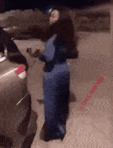 a woman in a blue dress is standing next to a car and holding a cell phone .