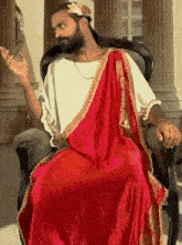 a man dressed as a roman emperor is sitting in a chair with his hands outstretched