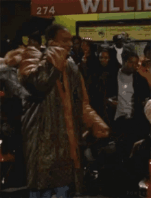 a man in a leather jacket is standing in a crowd of people in front of a store that says 274
