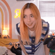 a woman with orange hair is smiling while standing in front of a camera in a room .
