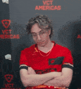 a man in a red shirt is sitting in front of a wall that says vct americas