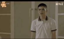 a young man in a white shirt is standing in front of a window with netflix written on the bottom of the screen