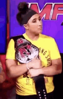 a woman wearing a yellow shirt is holding a wrestling belt .