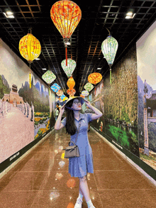 a woman in a blue dress stands in a hallway with lanterns on the ceiling