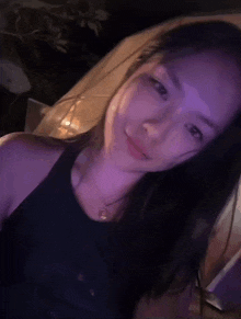 a woman in a black tank top is smiling in a dark room with purple lights .