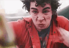 a man in a red shirt is making a funny face and pointing at the camera .