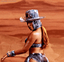a woman in a bikini and cowboy hat is sitting on the ground in the desert .